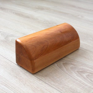 May include: A wooden half-round cylinder, also known as a bolster, is made of light brown wood. It is a yoga prop used for stretching and support.