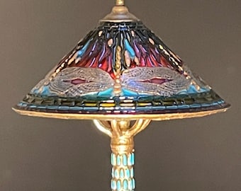 Pode incluir: Um abajur de mesa com um abajur de vidro colorido com um design de libélula. O abajur é uma mistura de vidro roxo, azul e verde. A base é de metal dourado com um design de padrão azul e dourado.