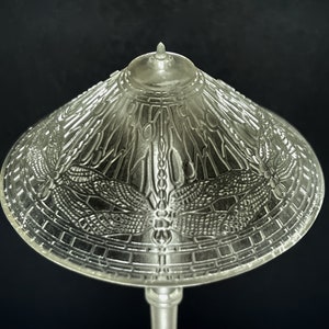 Op de afbeelding: Een heldere glazen tafellamp met een libellenontwerp op de kap. De lamp heeft een zilveren voet en een witte kap.