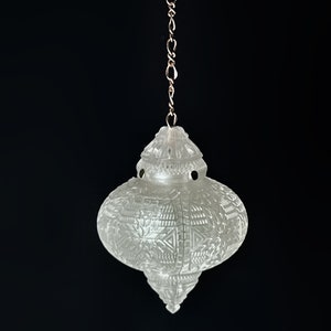 May include: A white, ornate, hanging pendant light fixture with a chain and a decorative top. The light fixture has a geometric pattern.