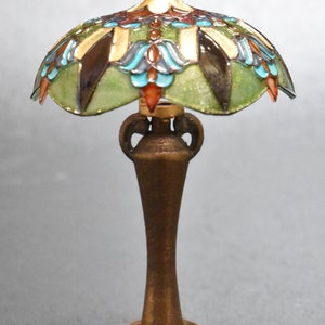 K&ouml;nnte beinhalten: Eine Miniatur-Lampe aus Buntglas mit einem gr&uuml;nen, blauen und goldenen Design. Die Lampe hat einen bronzenen Sockel mit einem dekorativen Blumenmuster.