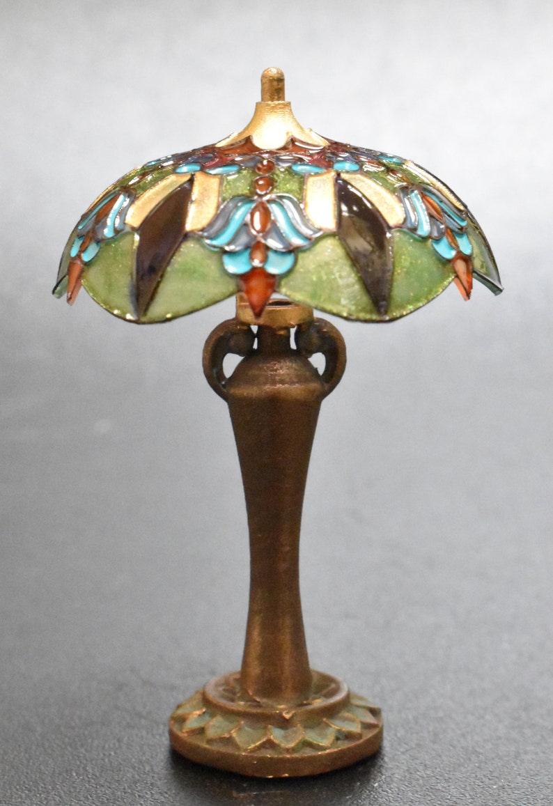K&ouml;nnte beinhalten: Eine Miniatur-Lampe aus Buntglas mit einem gr&uuml;nen, blauen und goldenen Design. Die Lampe hat einen bronzenen Sockel mit einem dekorativen Blumenmuster.