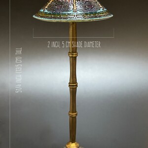 Op de afbeelding: Een gouden tafellamp met een gebrandschilderd lampenkap met een libellenmotief. De lampenkap heeft een diameter van 5 cm en de lamp is 13,5 cm hoog.
