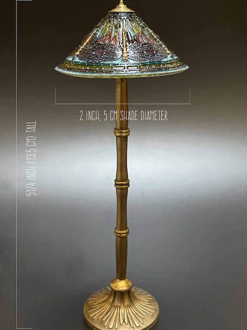 Op de afbeelding: Een gouden tafellamp met een gebrandschilderd lampenkap met een libellenmotief. De lampenkap heeft een diameter van 5 cm en de lamp is 13,5 cm hoog.
