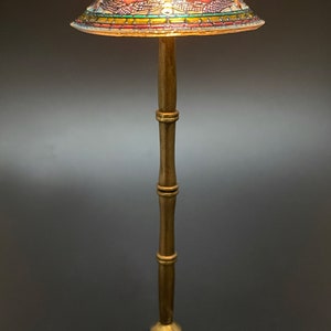 Op de afbeelding: Een gouden staande lamp met een gebrandschilderd lampenkap met een libellenmotief. De kap wordt verlicht door een warm licht.
