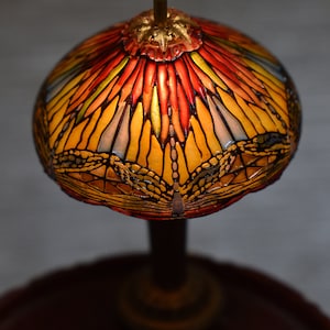 Pode incluir: Uma l&acirc;mpada de vitral com um design de lib&eacute;lula. O abajur &eacute; amarelo, laranja e vermelho com um contorno preto. A base &eacute; marrom escura.