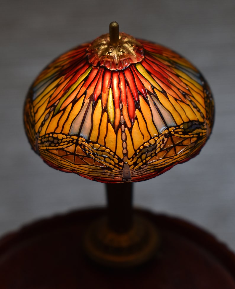 Pode incluir: Uma l&acirc;mpada de vitral com um design de lib&eacute;lula. O abajur &eacute; amarelo, laranja e vermelho com um contorno preto. A base &eacute; marrom escura.