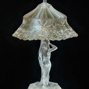 Può includere: Una lampada in vetro trasparente con un paralume in vetro smerigliato e una figura femminile scolpita come base.