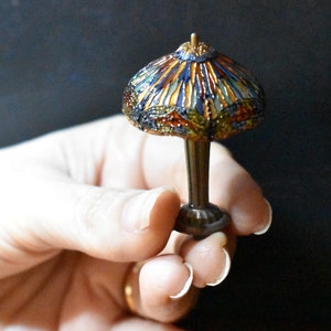 Pode incluir: Uma l&acirc;mpada de vidro Tiffany em miniatura com um design geom&eacute;trico colorido. A l&acirc;mpada &eacute; feita de vidro e metal e tem uma base marrom escura.