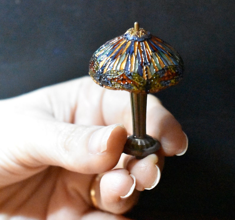 Pode incluir: Uma l&acirc;mpada de vidro Tiffany em miniatura com um design geom&eacute;trico colorido. A l&acirc;mpada &eacute; feita de vidro e metal e tem uma base marrom escura.