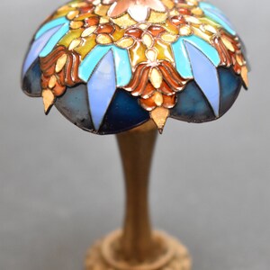 K&ouml;nnte beinhalten: Eine Miniatur-Lampe aus Buntglas mit einem blauen, t&uuml;rkisfarbenen, orangefarbenen und goldenen Design. Die Lampe hat einen goldenen Sockel.