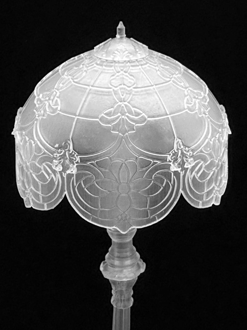 May include: A clear, ornate lamp with a domed shade featuring floral and geometric patterns. The lamp has a detailed base and stem, showcasing a vintage design. The shade's design is reminiscent of stained glass.