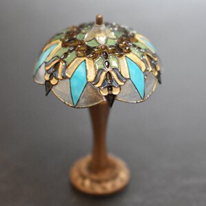 K&ouml;nnte beinhalten: Eine Miniatur-Lampe aus Buntglas mit einem t&uuml;rkisfarbenen, goldenen und gr&uuml;nen Design. Die Lampe hat einen Holzsockel.