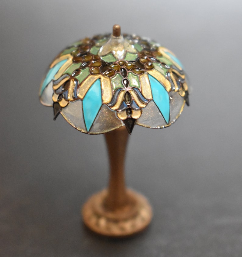 K&ouml;nnte beinhalten: Eine Miniatur-Lampe aus Buntglas mit einem t&uuml;rkisfarbenen, goldenen und gr&uuml;nen Design. Die Lampe hat einen Holzsockel.