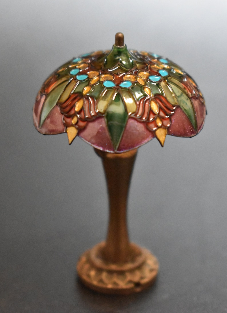 K&ouml;nnte beinhalten: Eine Miniatur-Lampe aus Buntglas mit goldener Basis. Der Lampenschirm zeigt ein florales Design in den Farben Rosa, Gr&uuml;n, Gold und T&uuml;rkis.