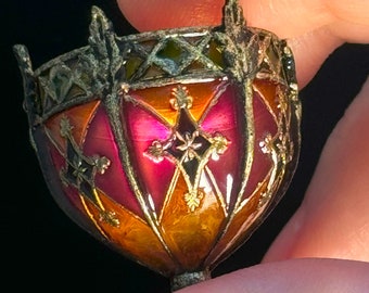 Könnte beinhalten: Eine kleine, verzierte, farbige Glaslampe mit einem roten, orangen und violetten Farbschema. Die Lampe hat einen Metallrahmen und komplizierte Details.
