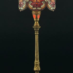 May include: A decorative floor lamp with a stained glass shade. The shade features a floral design in shades of orange, red, and pink. The lamp has a brass-colored base and stem, and stands approximately 60 inches tall.