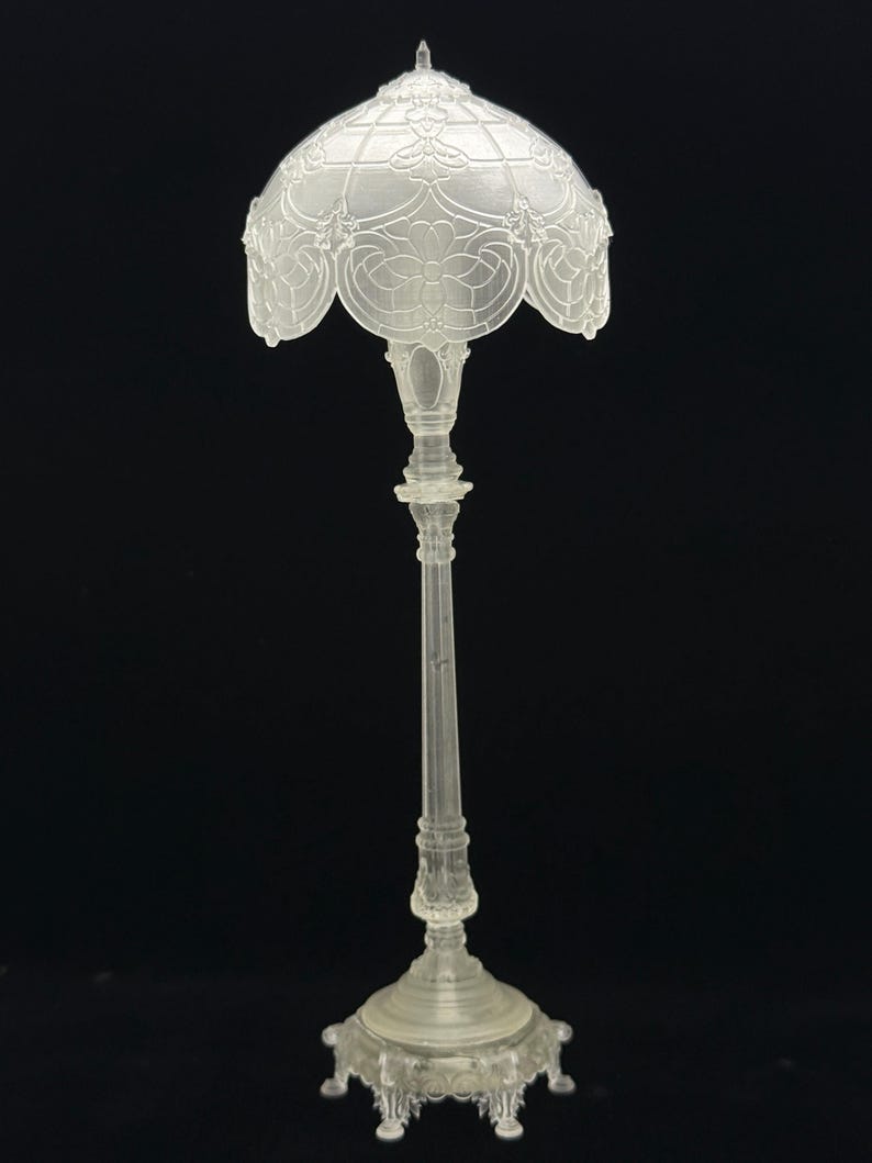 May include: A clear, ornate lamp with a detailed floral design on the shade. The lamp has a tall, slender stem and a decorative base. The shade is approximately 6 inches in diameter.