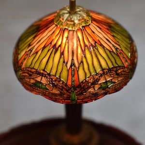 Pode incluir: Um abajur de vidro colorido com um design de lib&eacute;lula em tons de verde, laranja e marrom. O abajur &eacute; iluminado por dentro, criando um brilho quente.