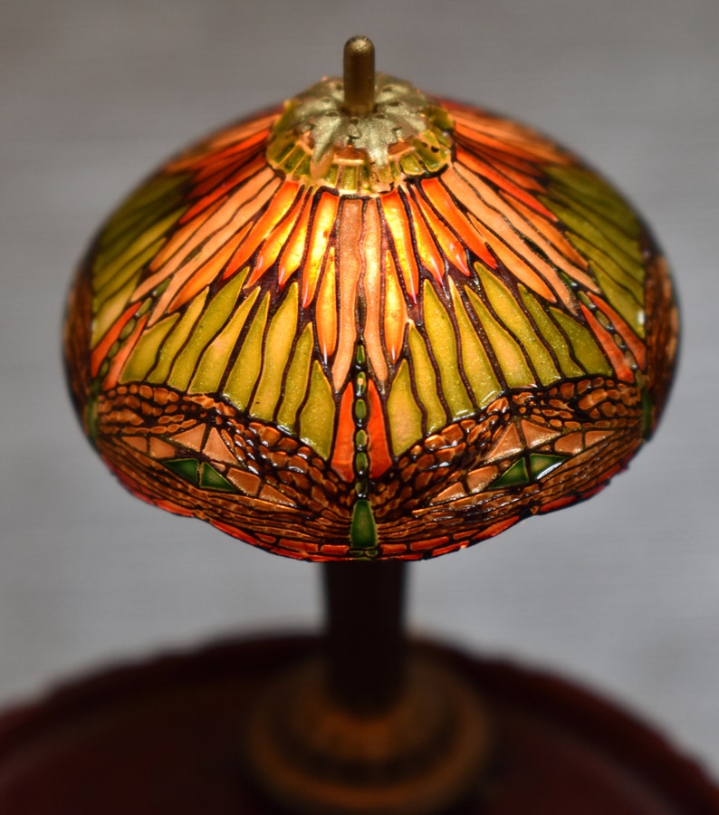 Pode incluir: Um abajur de vidro colorido com um design de lib&eacute;lula em tons de verde, laranja e marrom. O abajur &eacute; iluminado por dentro, criando um brilho quente.