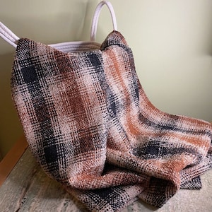 May include: A brown, black and white plaid throw blanket draped over a white wicker basket.