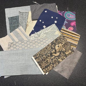 May include: A collection of fabric swatches in various patterns and colors, including gray, blue, brown, beige, and white. The fabrics feature geometric, floral, and paisley designs.