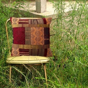 May include: A decorative throw pillow with a patchwork design featuring brown, red, and gold tones. The pillow has a geometric pattern with circles and stripes.