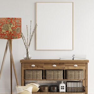May include: A wooden tripod floor lamp with a red lampshade featuring a gold elephant and floral pattern, a large empty rectangular picture frame, and a wooden console table with three drawers, three wicker baskets, and decor items.