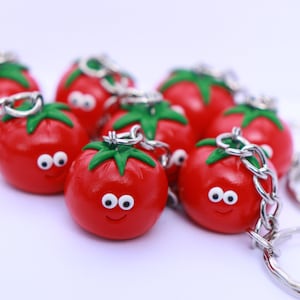 May include: A group of eight red tomato-shaped keychains with green stems and white eyes. Each keychain has a silver metal ring.