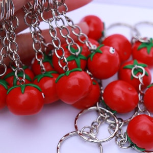 May include: A set of red tomato keychain charms with green stems and silver key rings. The charms are attached to silver chains.