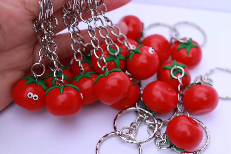 May include: A set of red tomato keychain charms with green stems and silver key rings. The charms are attached to silver chains.