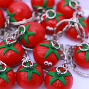 May include: A collection of red tomato-shaped keychains with green leaves and silver key rings. The keychains are made of a soft, pliable material and have a realistic appearance.