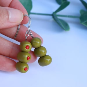 Puede incluir: Un par de pendientes en forma de oliva con centros rojos. Los pendientes están hechos de arcilla polimérica y están unidos a ganchos plateados.