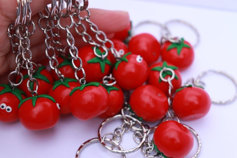 May include: A group of red tomato-shaped keychains with green stems and silver key rings. The keychains are attached to silver chains.