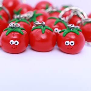 May include: A group of red tomato-shaped keychains with green stems and white eyes. The keychains have a smiling face and are attached to silver key rings.