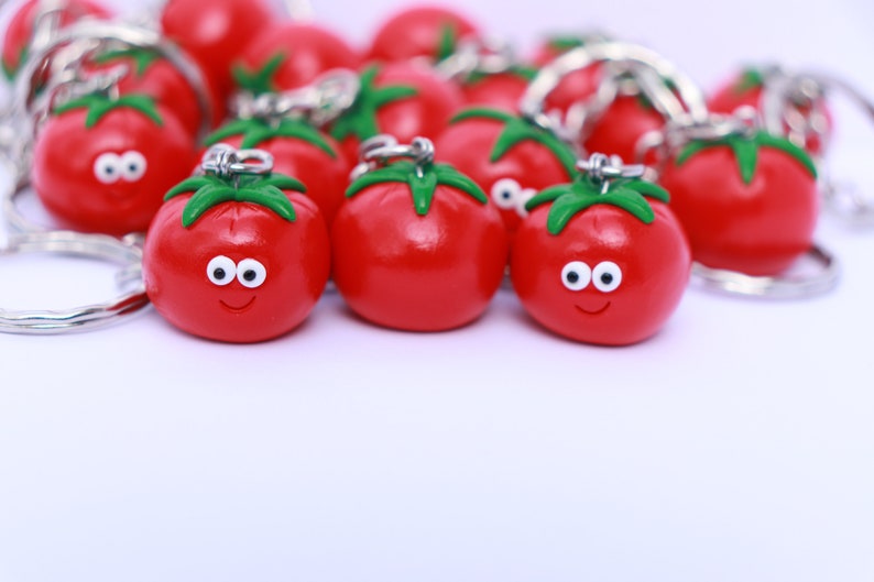 May include: A group of red tomato-shaped keychains with green stems and white eyes. The keychains have a smiling face and are attached to silver key rings.
