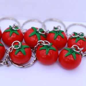 May include: A set of nine red tomato keychain charms with green leaves. Each charm is attached to a silver key ring.