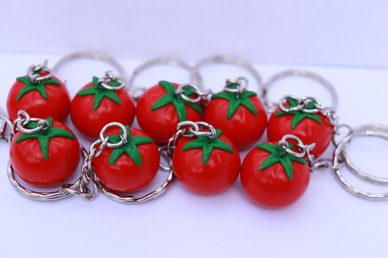 May include: A set of nine red tomato keychain charms with green leaves. Each charm is attached to a silver key ring.