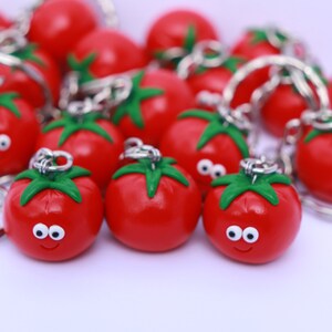 May include: A group of red tomato-shaped keychains with green stems and white eyes. The keychains are attached to silver key rings.