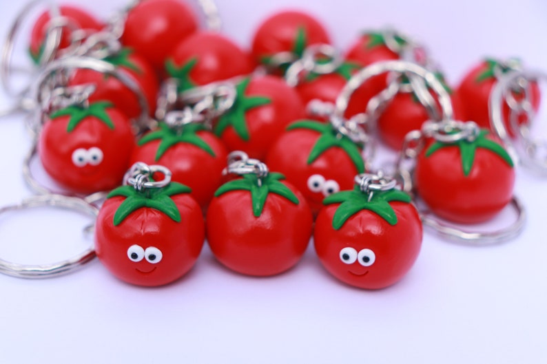 May include: A group of red tomato-shaped keychains with green stems and white eyes. The keychains are attached to silver key rings.
