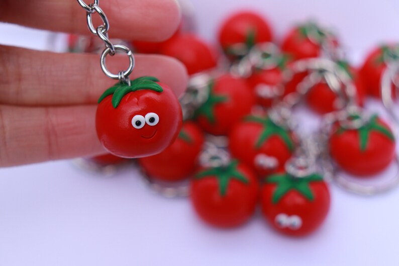 May include: A keychain featuring a red tomato with a green stem and a smiling face. The tomato is attached to a silver chain with other red tomato keychains.