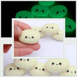 May include: A collection of small, oval-shaped, off-white figurines with smiling faces. The figurines have black eyes and pink cheeks. Some glow green in the dark. The figurines are shown in a hand and on a white surface.