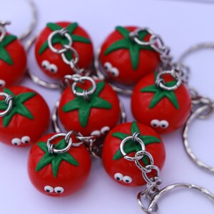 May include: A group of eight red tomato-shaped keychains with green leaves and googly eyes. Each keychain has a silver metal ring and chain.