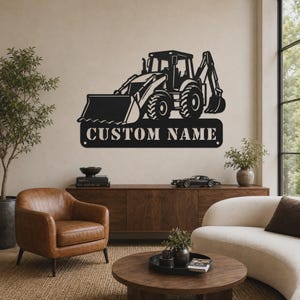 May include: A black metal wall sign featuring a silhouette of a backhoe loader construction vehicle. Below the vehicle, a rectangular plate displays the text CUSTOM NAME in bold, capital letters. The sign has two small circular mounting holes.