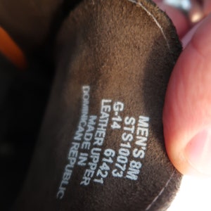 May include: Close-up of a brown leather shoe label with white text. The label reads "Men's 8M STS10073 G-14 61421 Leather Upper Made in Dominican Republic."