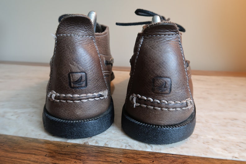 May include: A pair of brown leather boat shoes with a white stitching detail and a black rubber sole. The shoes have a logo on the side.