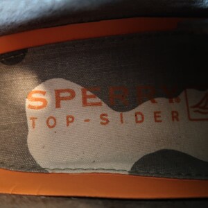 May include: Close-up of the inside of a shoe showing the Sperry Top-Sider logo with a small sailboat graphic.