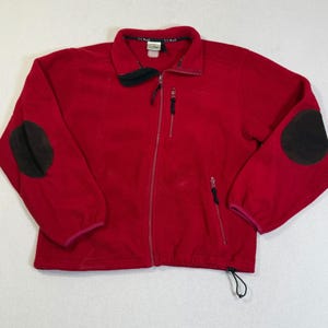 May include: A red fleece jacket with a full zip, two side pockets, and black elbow patches. The jacket has a stand-up collar and a drawstring at the hem. The L.L.Bean logo is visible on the chest.