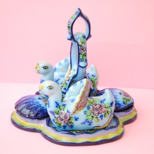 May include: A set of blue and white ceramic swan-shaped salt and pepper shakers with floral designs. The shakers are arranged on a matching blue and white ceramic base with a handle.