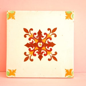 May include: A white ceramic tile featuring a red, orange and yellow floral design. The tile has a distressed look and is ideal for adding a touch of vintage charm to any space.